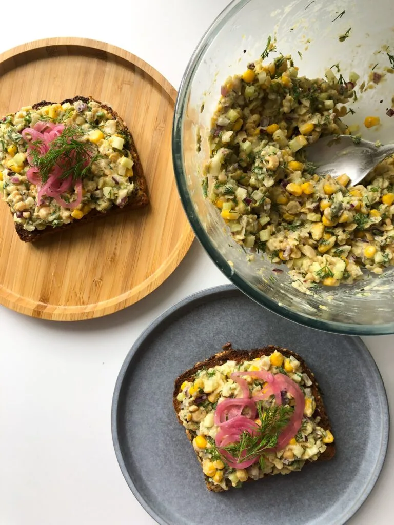 Chickpea Salad on a big glass bowl and spreaded in 2 slices of bread in two small plates topped with pickled red onion and dill