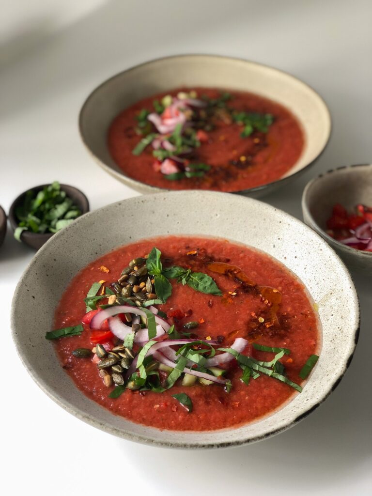 Gazpacho soup in two bowls with a topping of seeds and herbs