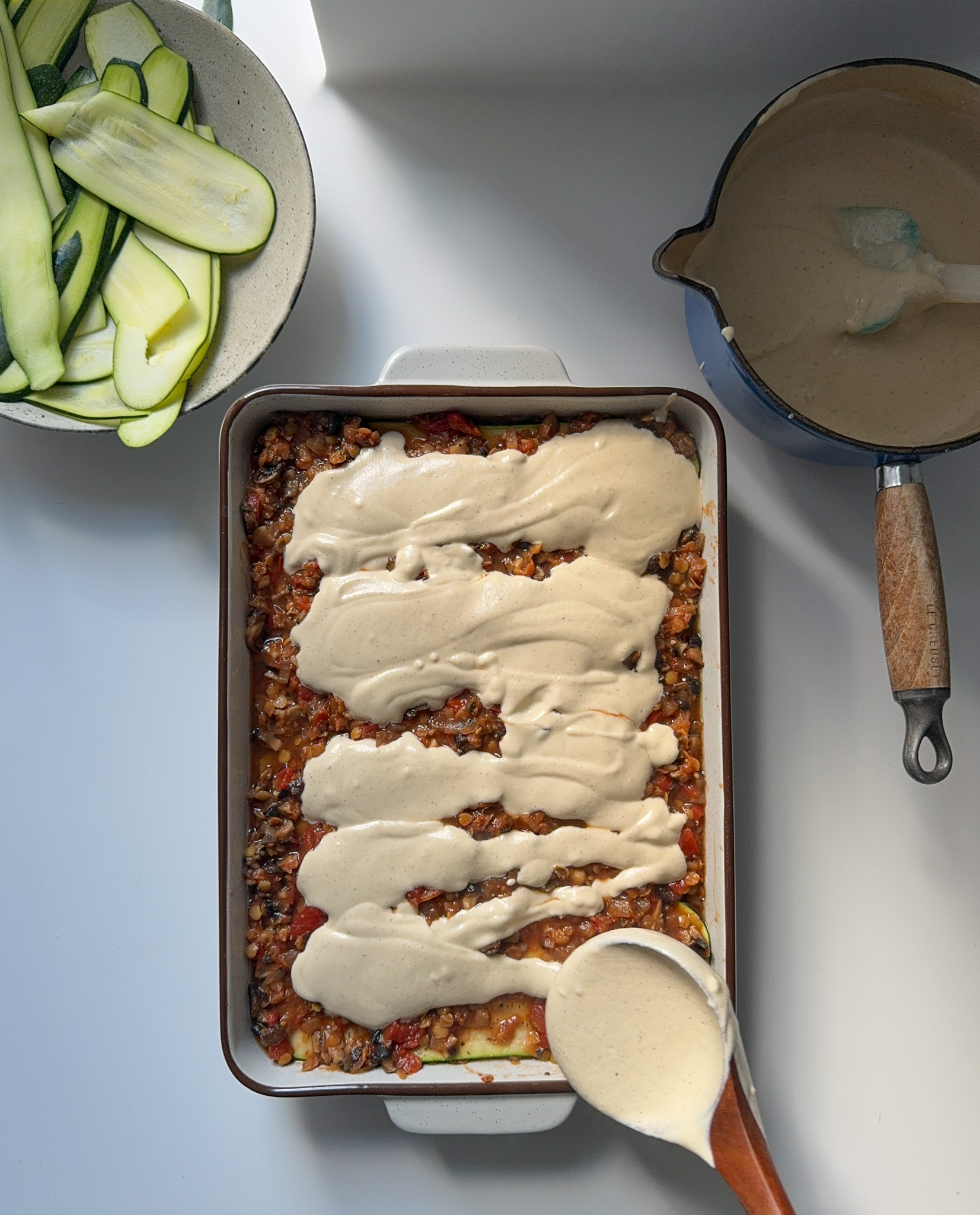 Spreading cashew Bechamel sauce on top of a Lasagne dish