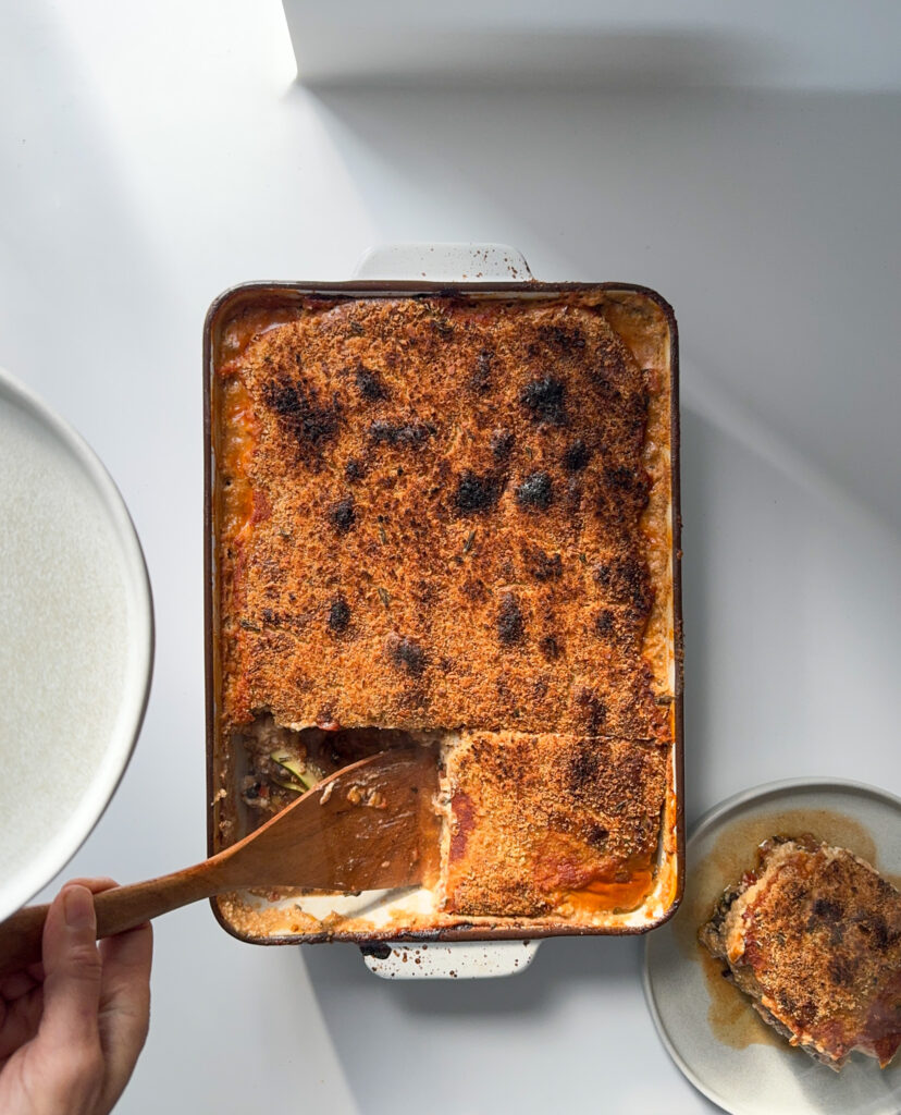 Golden lasagne being cut in squares and served in a round plate