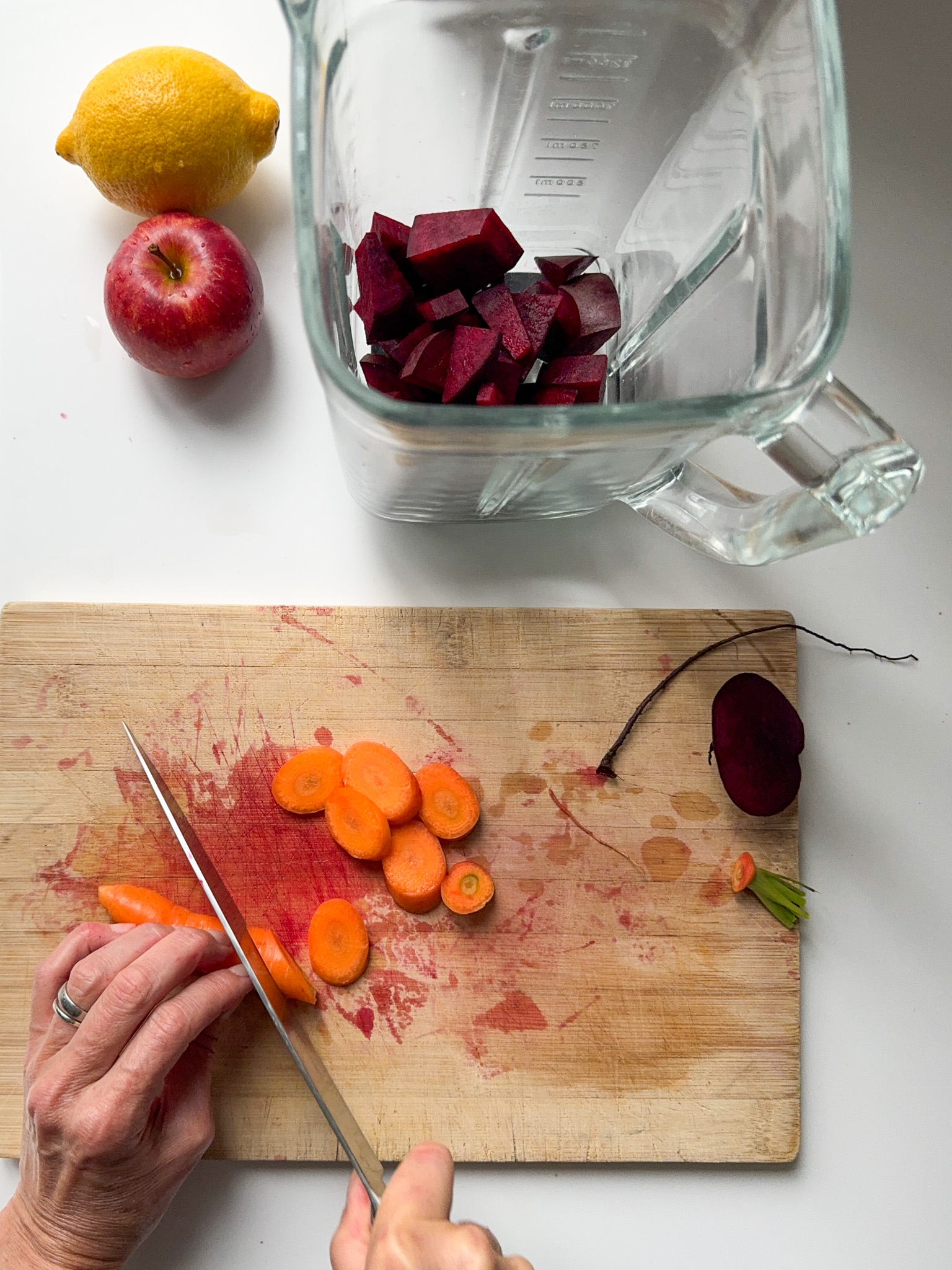 Cutting Carrots on a wood board. One apple, one lemon next to a blender with cut Beetroot