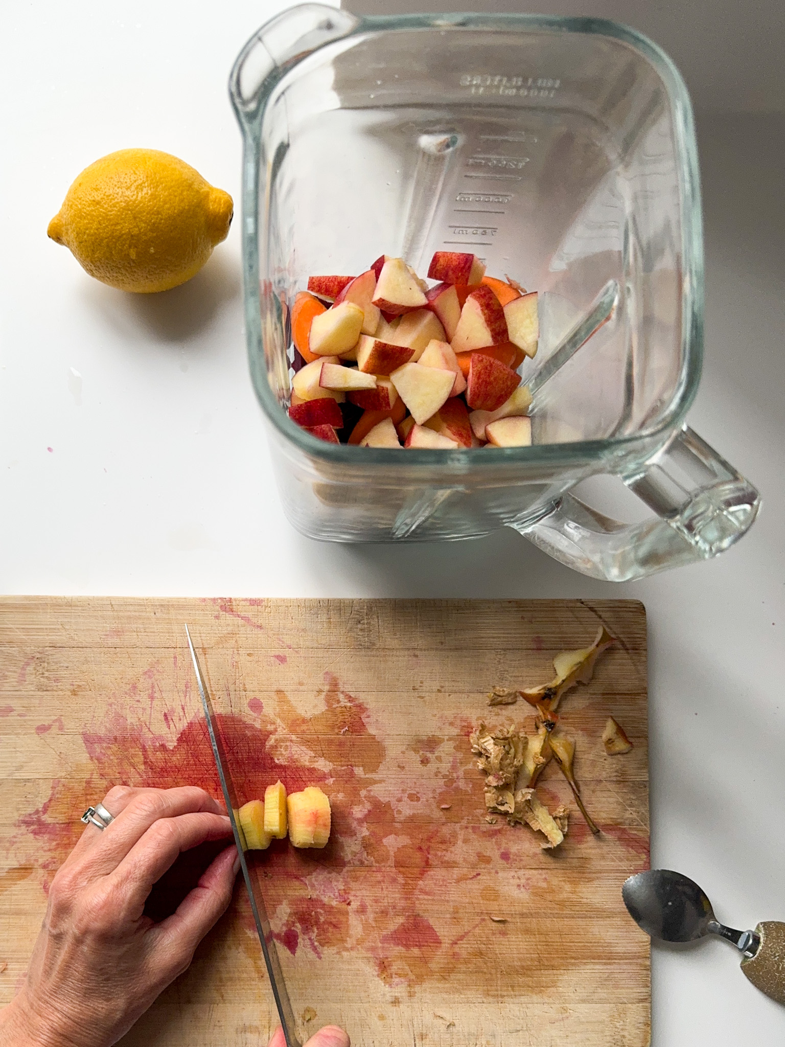 Cutting a piece of Ginger with a lemon next to a blender with cut beetroot and Apple