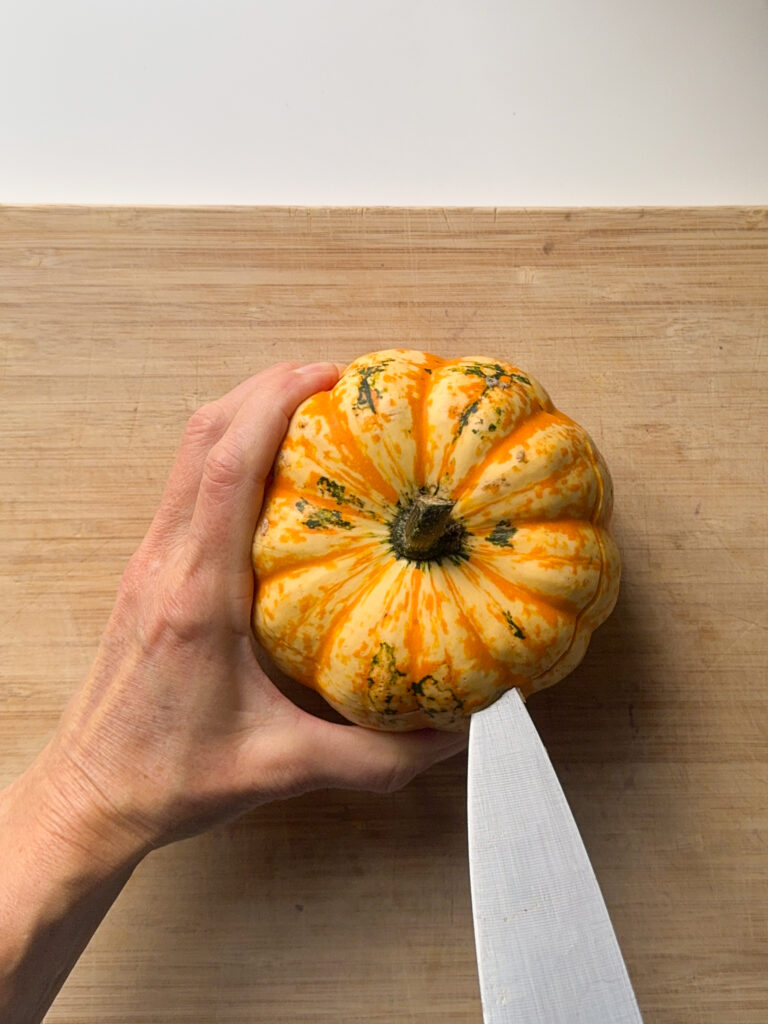 A carnival squash being cut with a big knife on a wood board