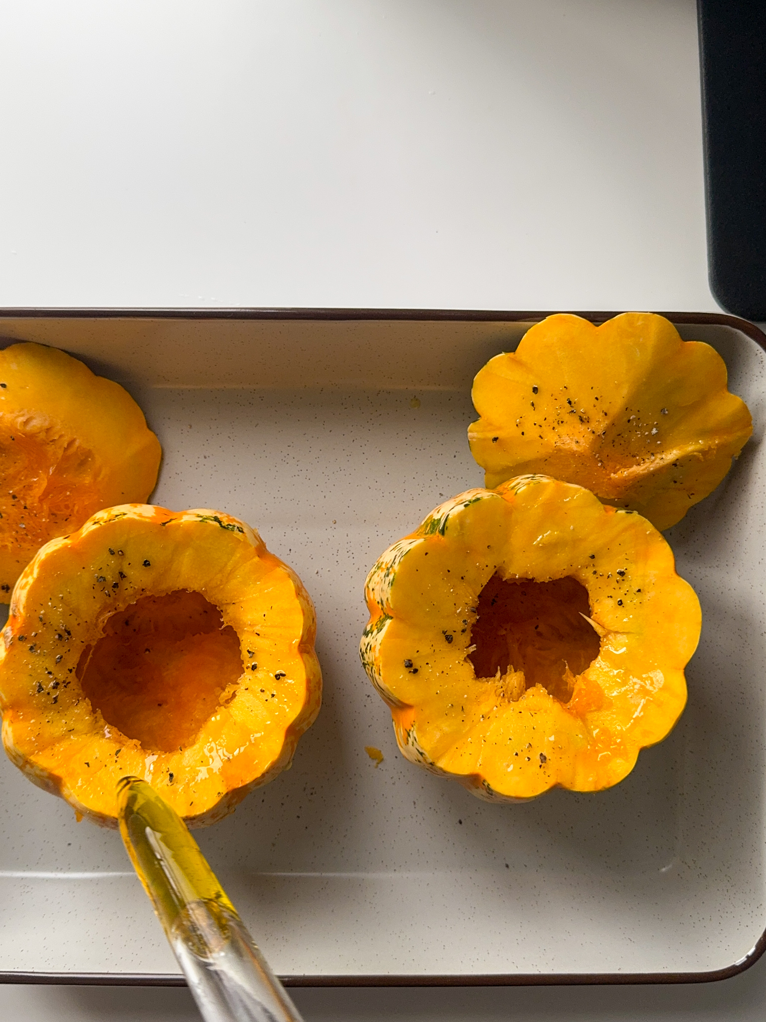 2 small pumpkins with the tops cut off, deseeded in a light grey trey being drizzled by Olive oil