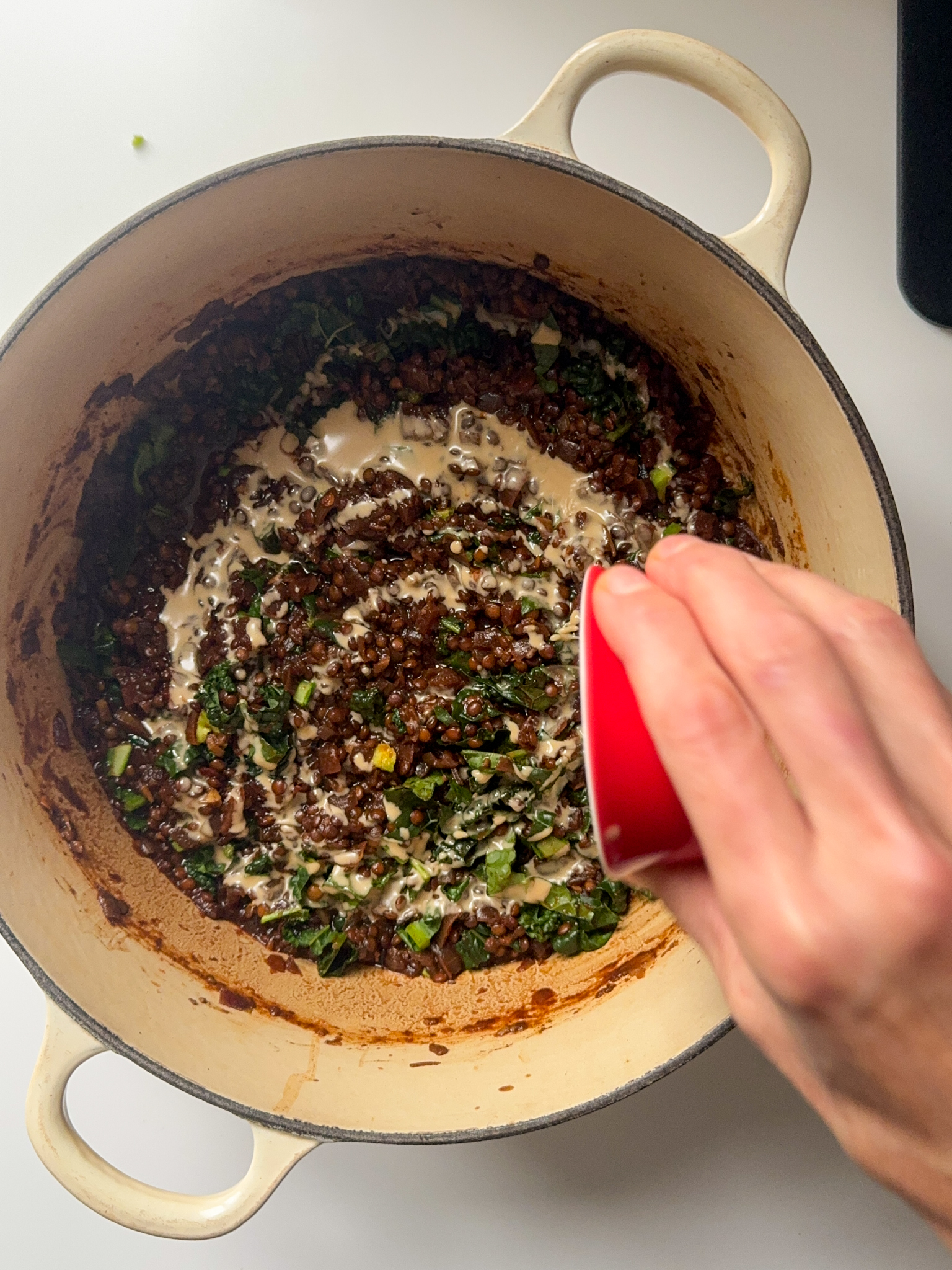 In a white dutch oven we can see a smoked beluga lentils being cooked and tahini being poor in