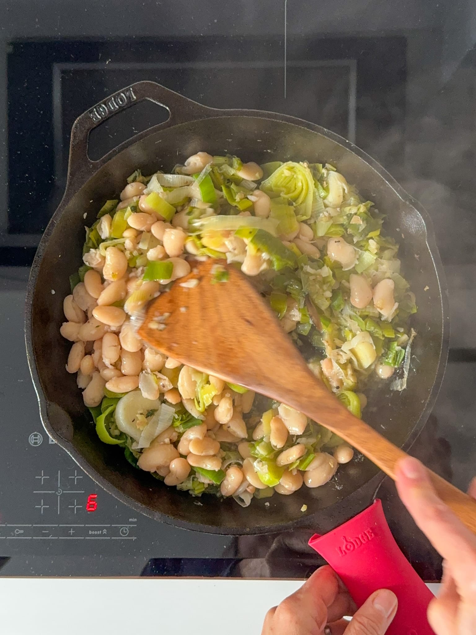 Leeks and butter beans being sauté in a cast iron pan