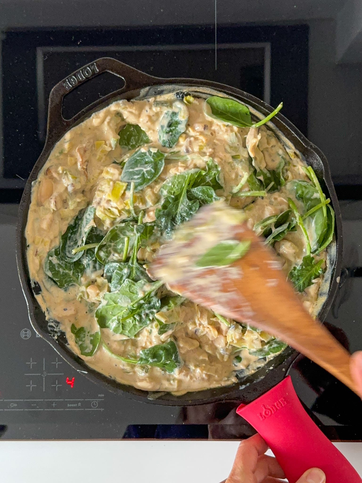 Spinach being added to a pan of creamy,cheese leek and butter bean mixture.