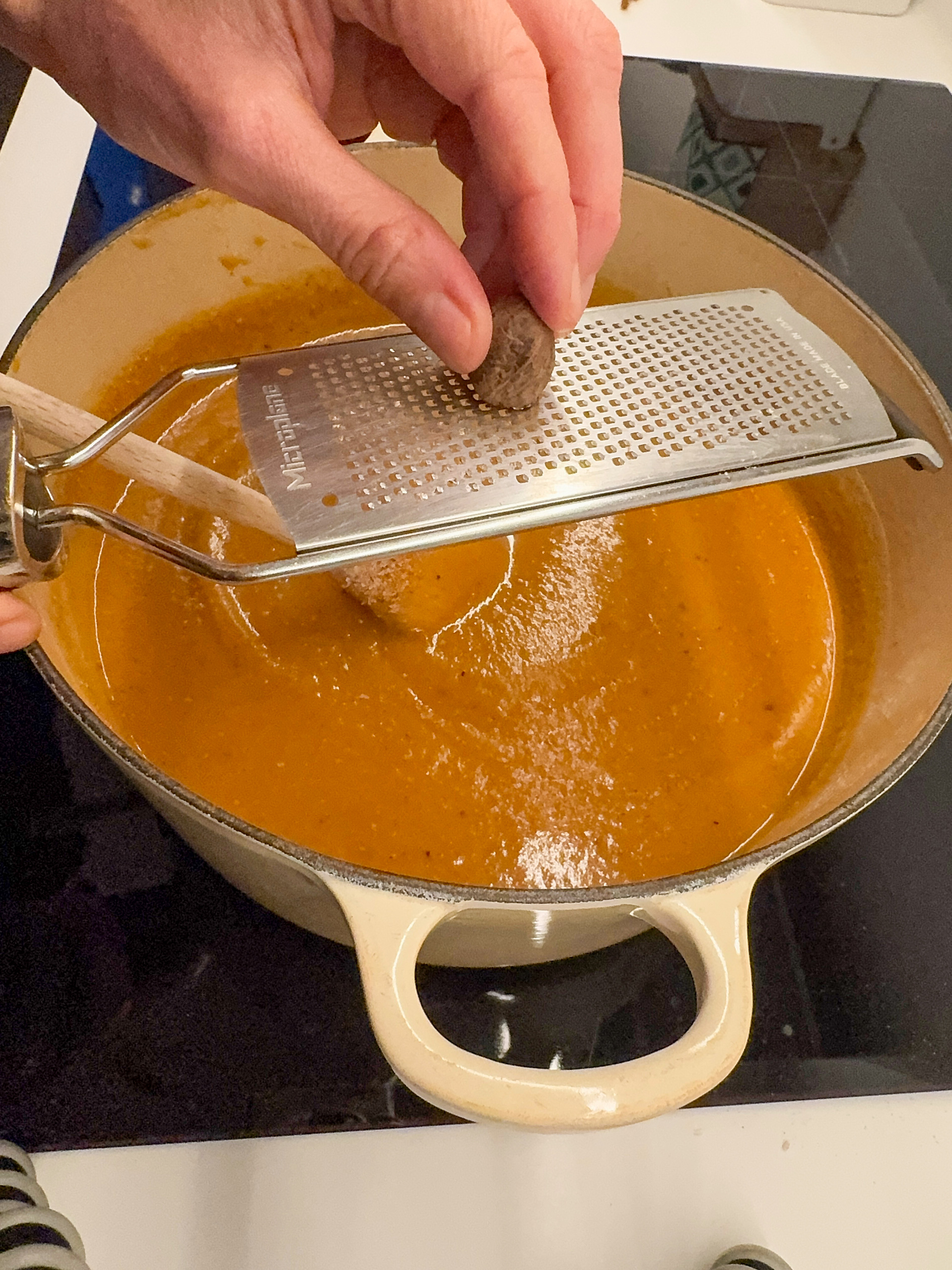 Grating nutmeg into Butternut squash soup in a white pot.