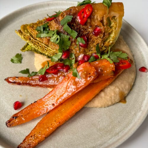 Savoy cabbage wedge on a butter bean mash with roast carrots. Topped with pomegranate seeds, slices of red chilli and chopped coriander.