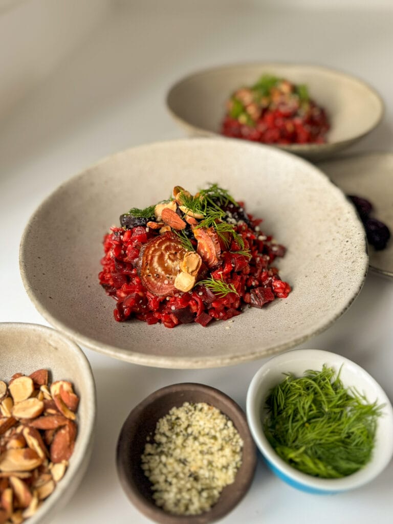 Roasted Beetroot Risotto on 2 bowls surrounded by little plates with Dill, Roasted Almonds, Hemp hearts