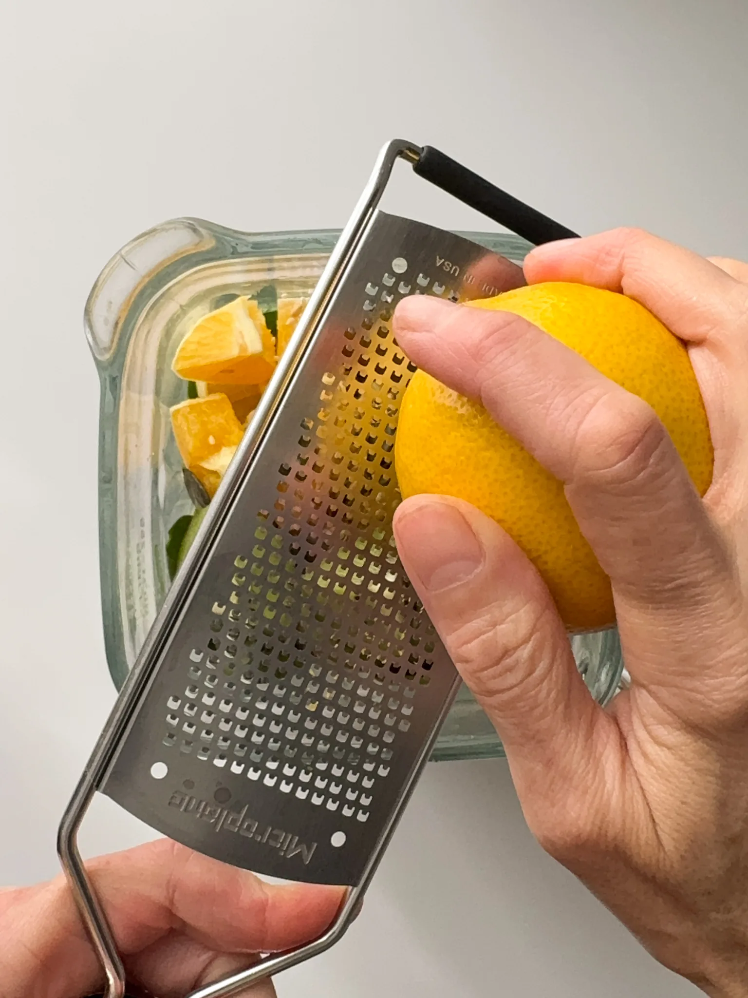 Grating Lemon zest into a glass jar fill with fruits and veggies