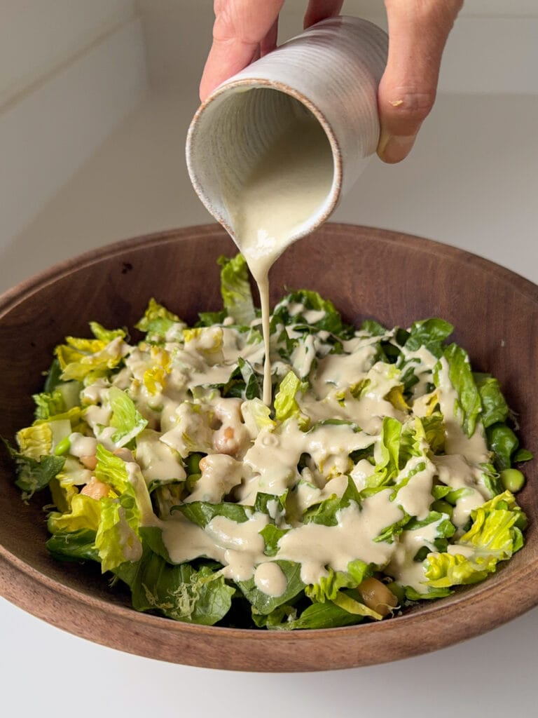 Healthy Vegan Caesar Salad Dressing being poured over a salad